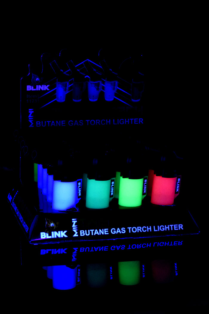 Dark-room shot of Blink Glow Mini Twisted 20-pack with tanks lit in blue, green, and red glow, countertop display view.