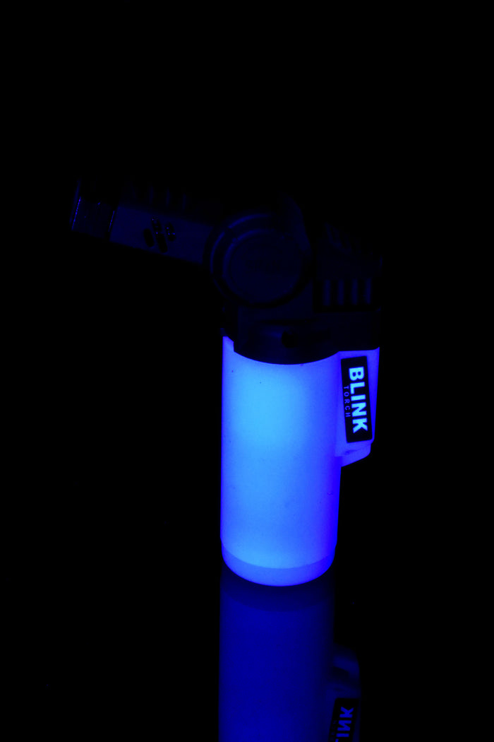 Single Blink Glow Mini Twisted lighter glowing blue in darkness with angled swivel nozzle and frosted tank, reflective surface.