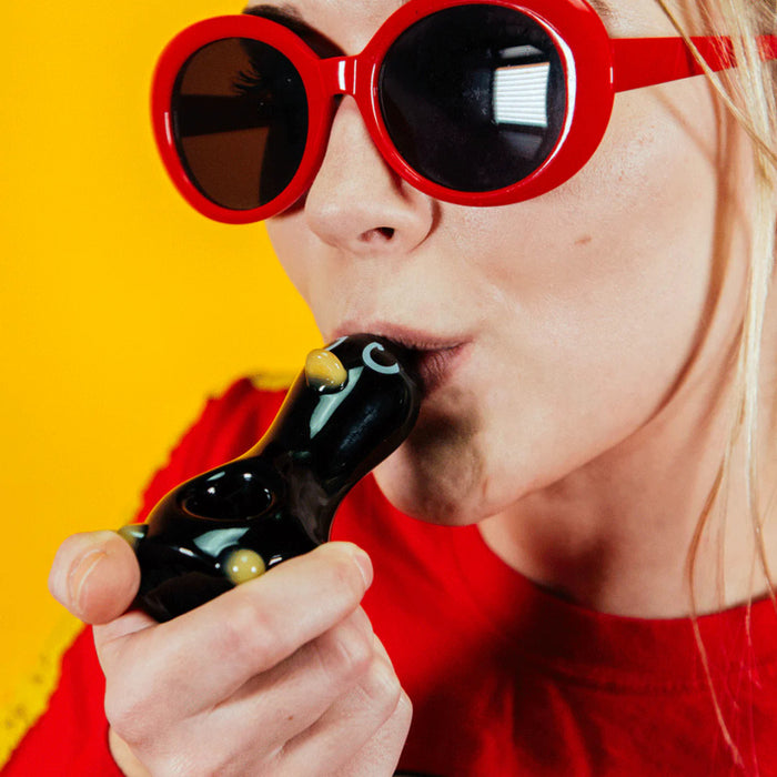 Person holding Goody Glass Penguin hand pipe with black body, white accents, and yellow feet