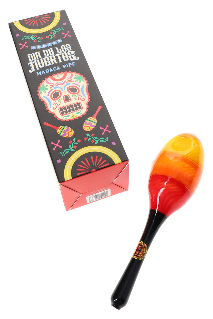 Hemper Dia De Los Muertos maraca glass hand pipe displayed next to colorful sugar-skull retail box on a clean white backdrop.