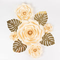 Cream paper flowers with gold leaves on a plain background