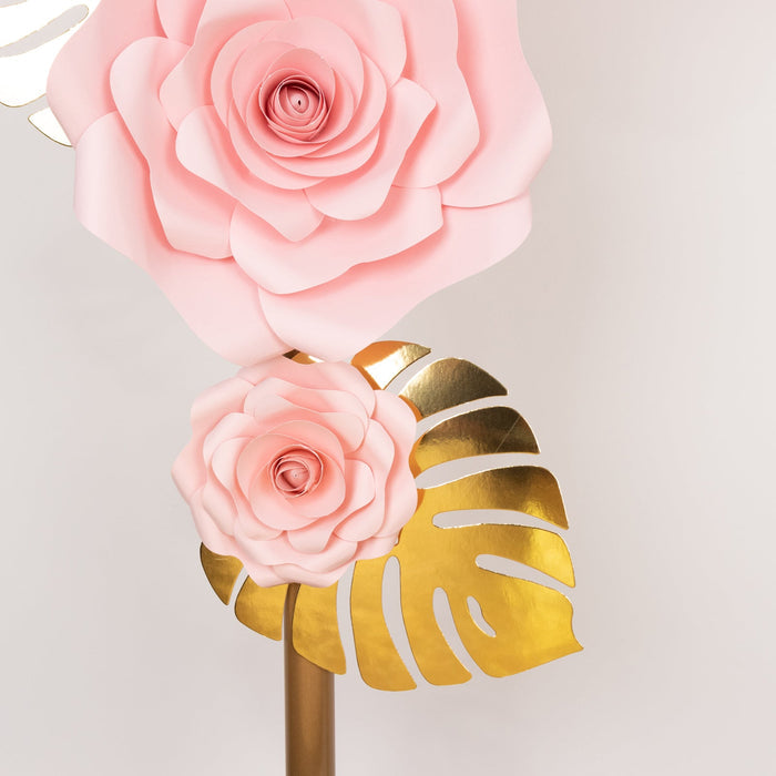 Pink paper flowers with gold leaves on a stand against a white backdrop.